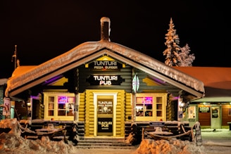 A cozy mountain lodge glowing warmly as night falls, with people enjoying drinks outside.