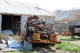 Old farm equipment with rusted metal parts lined up beside a barn.