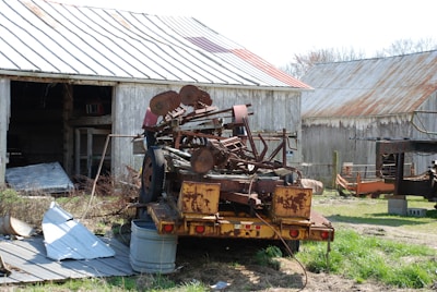 Old farm equipment with rusted metal parts lined up beside a barn.