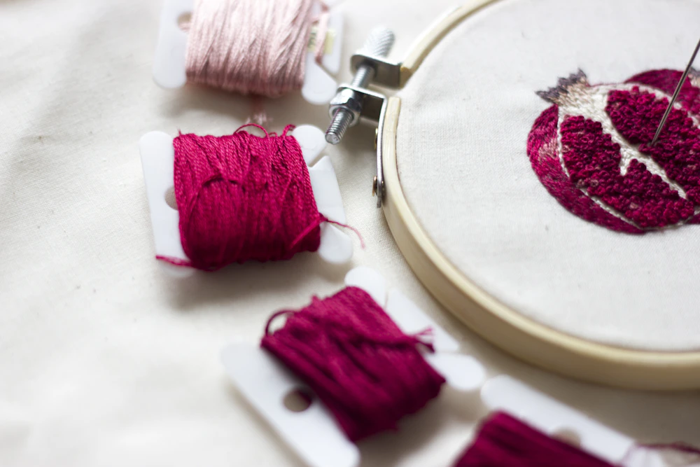 Embroidery hoop with pink thread and a work-in-progress design beside loose threads