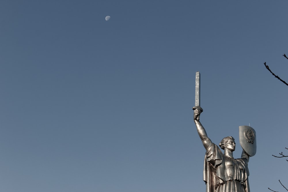 Homme tenant une statue d’épée sous le ciel bleu pendant la journée