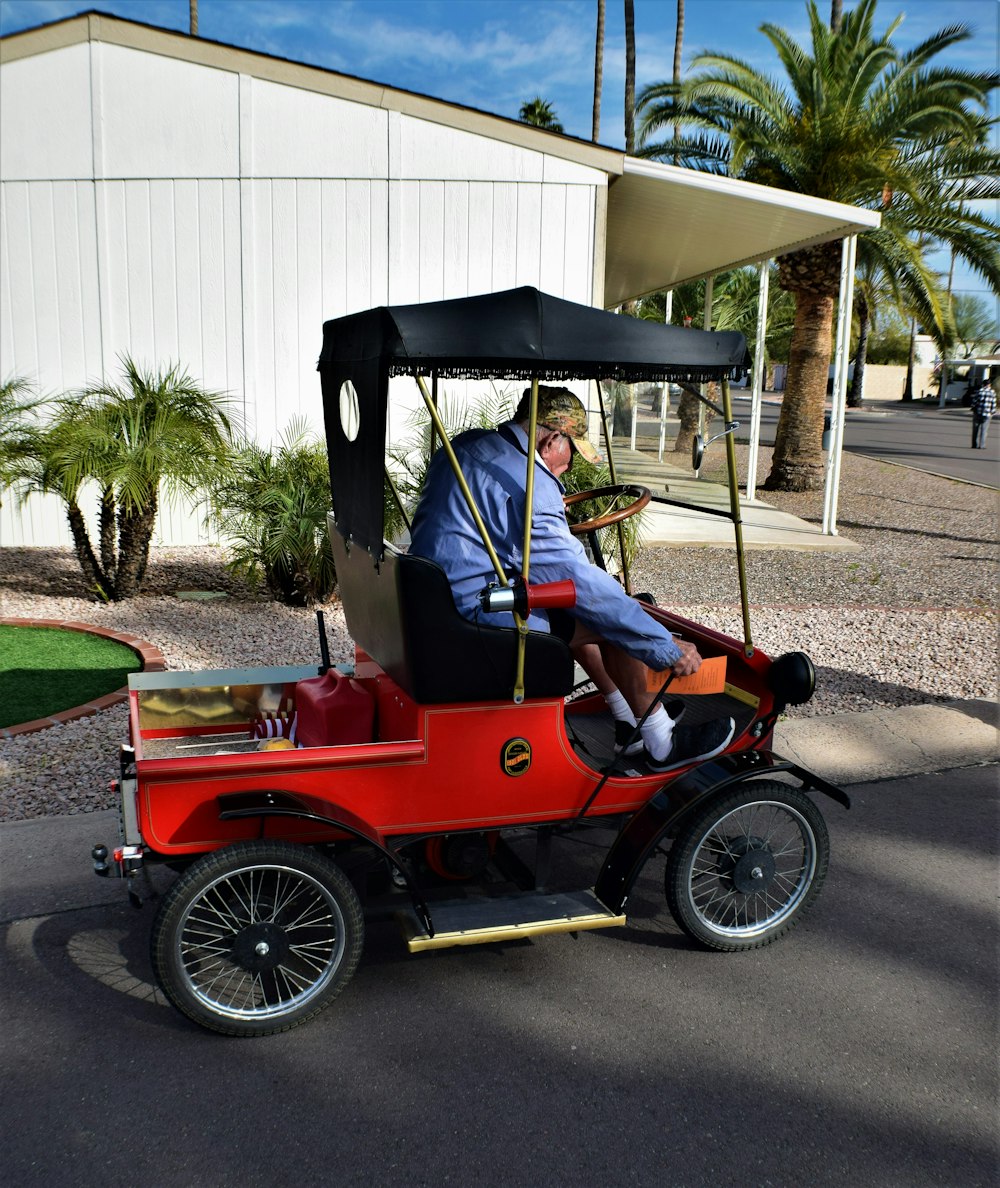 man in blue jacket riding red and black vintage car during daytime