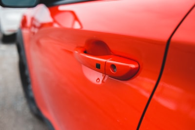 A modern automotive door handle mounted on a vibrant red hatchback.
