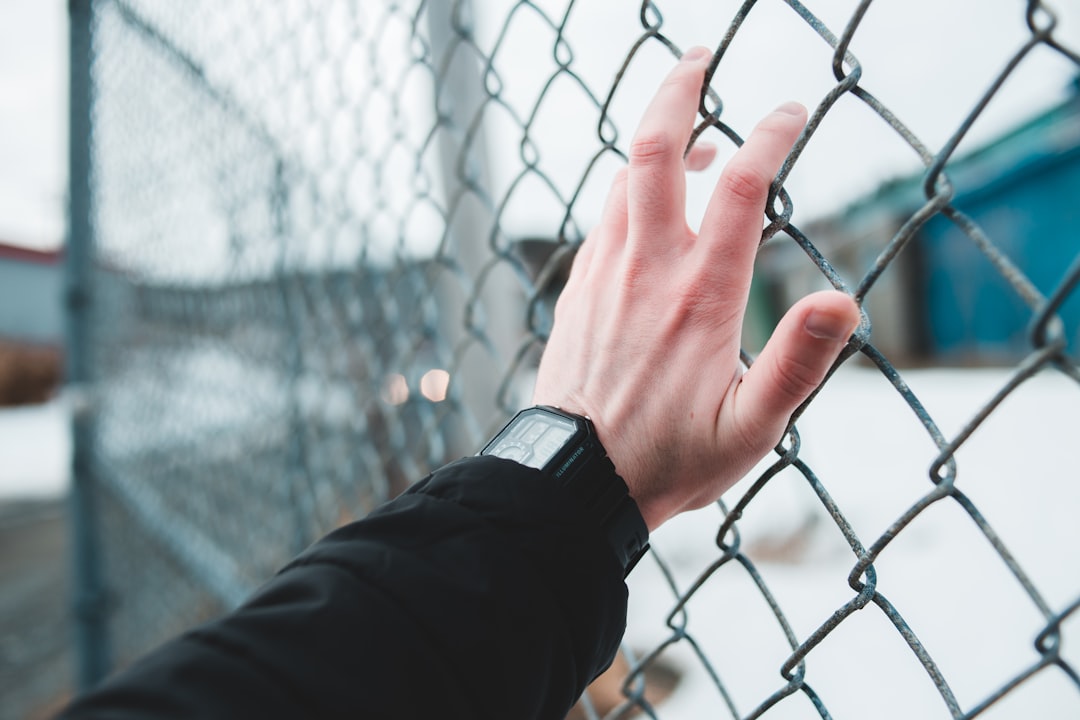 person wearing black watch holding gray metal fence