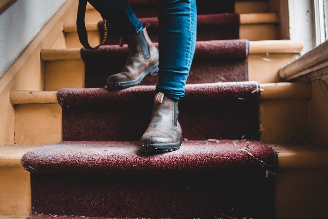 person in blue denim jeans and black leather boots sitting on red staircase