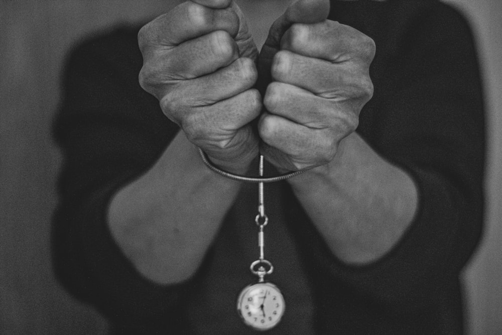 grayscale photo of person holding round pendant necklace