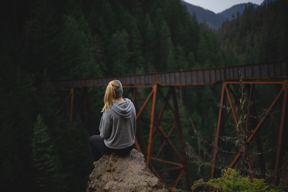 woman in gray long sleeve shirt sitting on brown rock during daytime