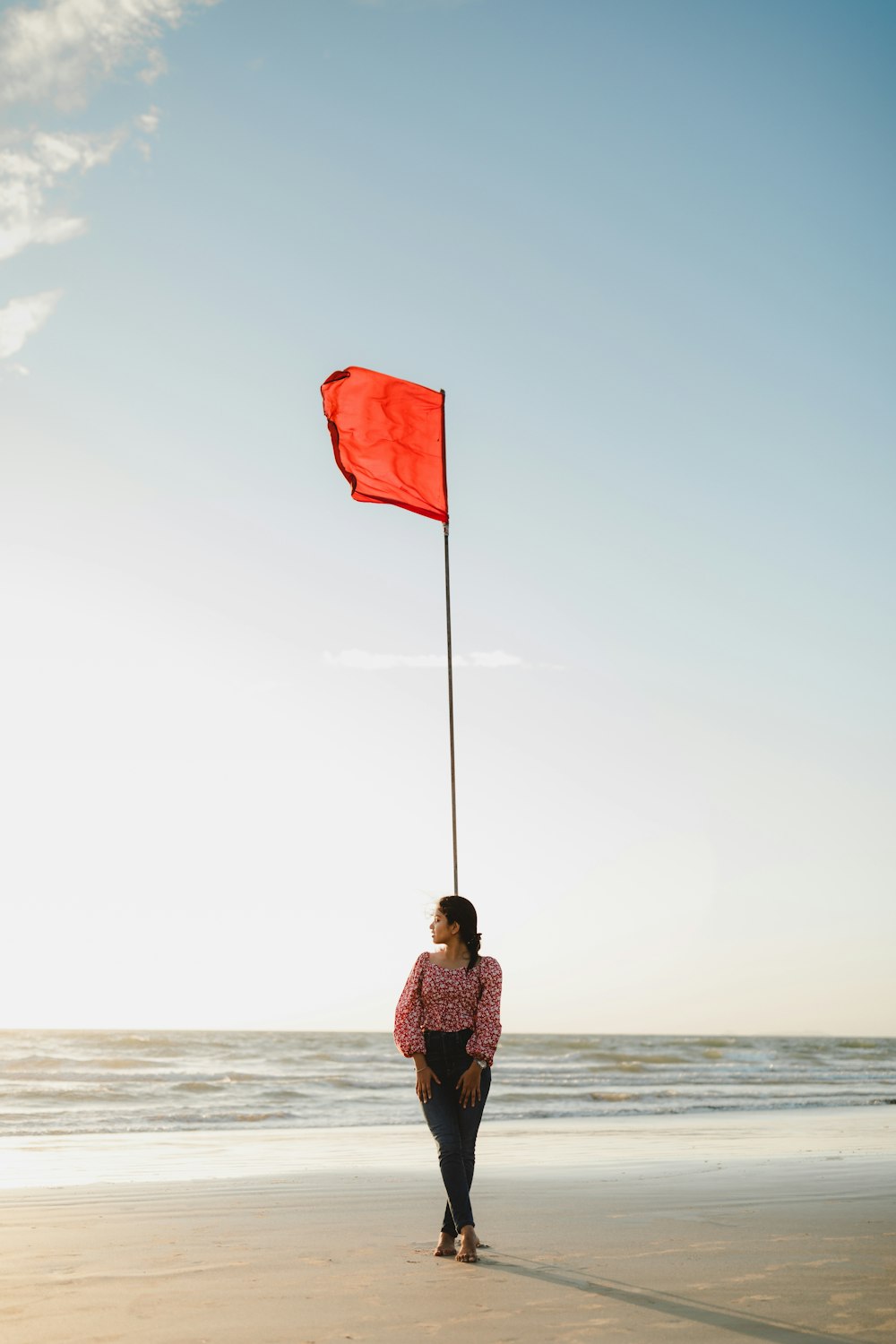 woman in brown jacket holding flag standing on beach shore during daytime