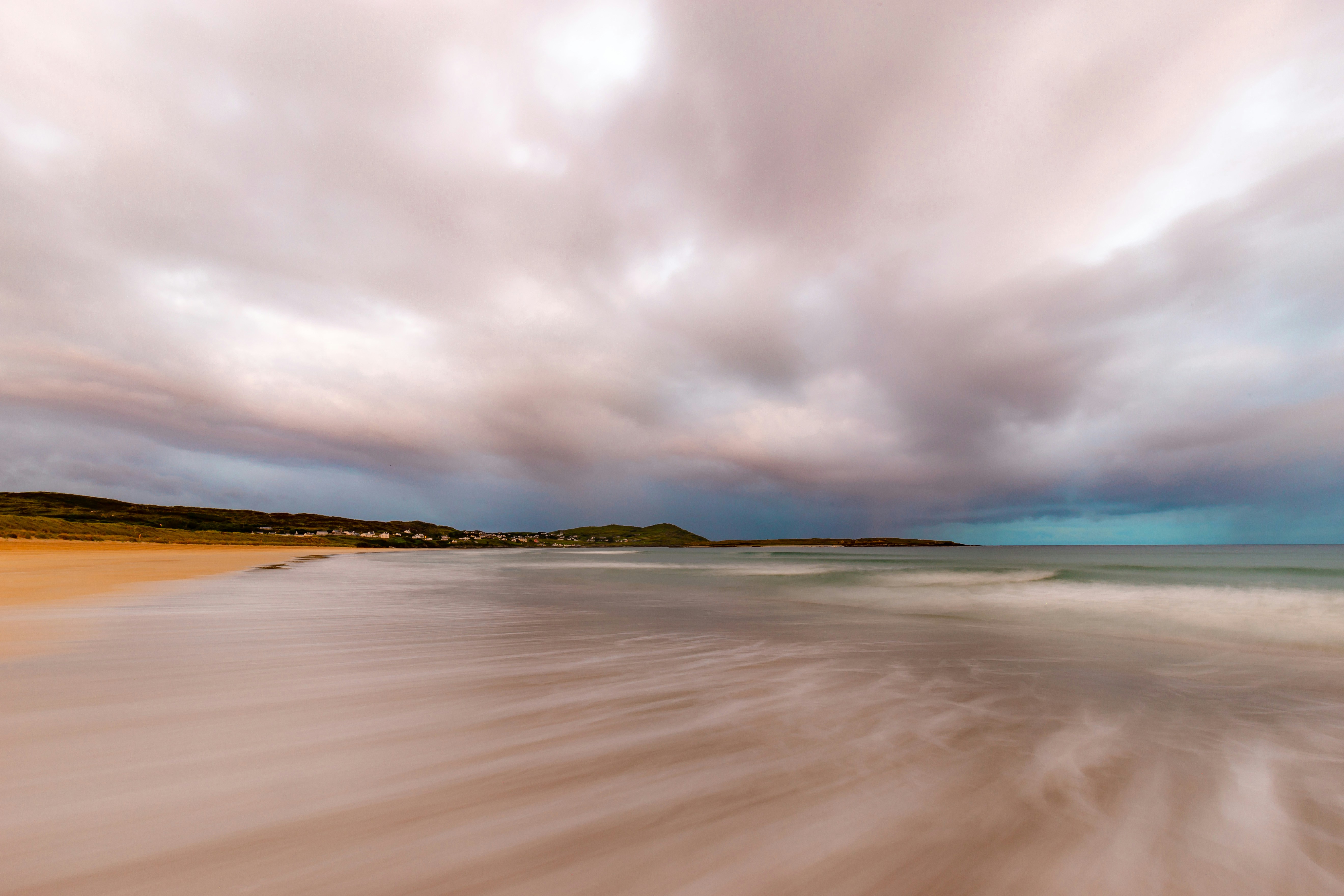 A calm beach scene at dusk with gentle waves and dramatic clouds