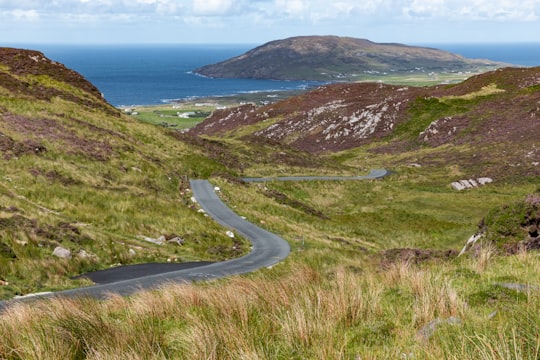 gray asphalt road on green mountain beside body of water during daytime in Donegal Ireland
