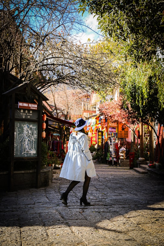 woman in white coat walking on sidewalk during daytime in Lijiang China