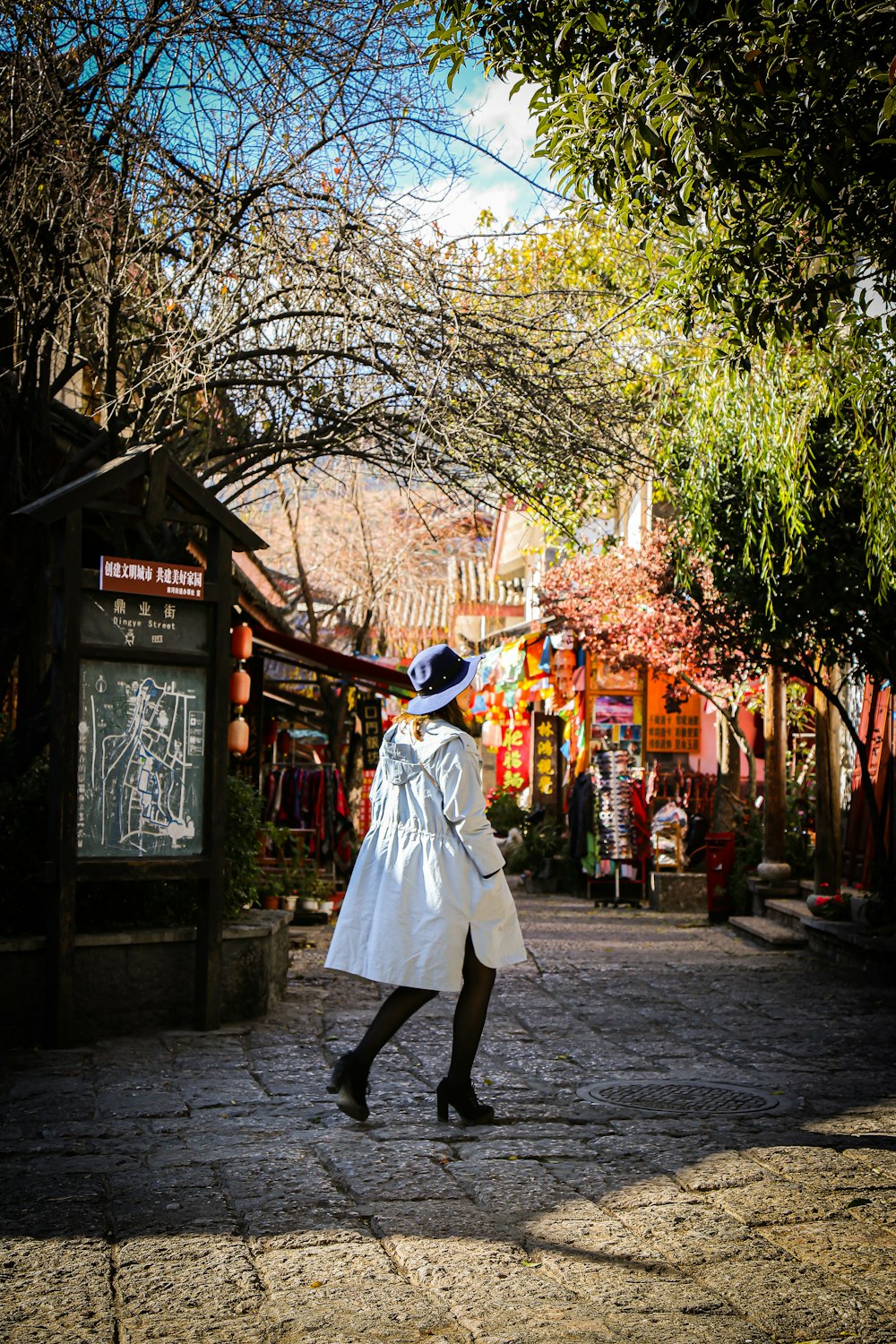 woman in white coat walking on sidewalk during daytime