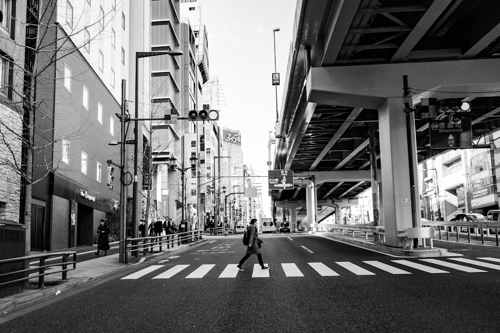 grayscale photo of man walking on sidewalk