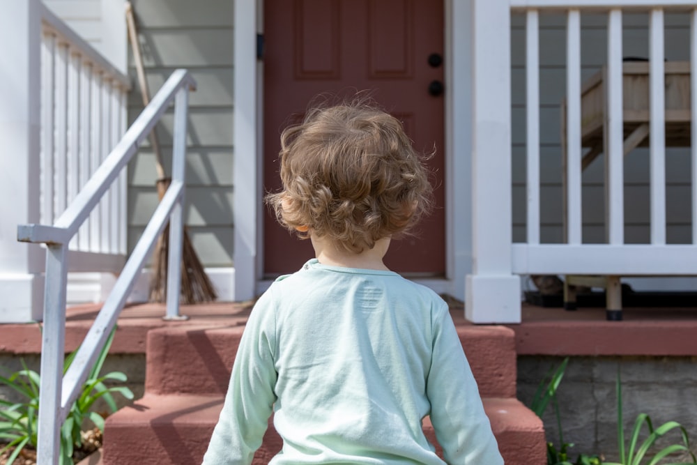 girl in teal long sleeve shirt standing on brown wooden stairs during daytime