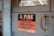 A worn, metal sign mounted on a wooden surface reads, 'A FIRE IN THIS BUILDING MIGHT PUT EVERY EMPLOYEE OUT OF WORK. Guard the Property Against Fire and Protect Your Job.' The sign features a bold black and red color scheme with a rustic backdrop.