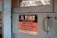 A worn, metal sign mounted on a wooden surface reads, 'A FIRE IN THIS BUILDING MIGHT PUT EVERY EMPLOYEE OUT OF WORK. Guard the Property Against Fire and Protect Your Job.' The sign features a bold black and red color scheme with a rustic backdrop.