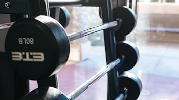 A set of gym weights is stacked on a rack near a bright window. The weights are arranged in descending order, with shiny metal bars connecting them. Natural light filters through the window, creating a calm and focused atmosphere.
