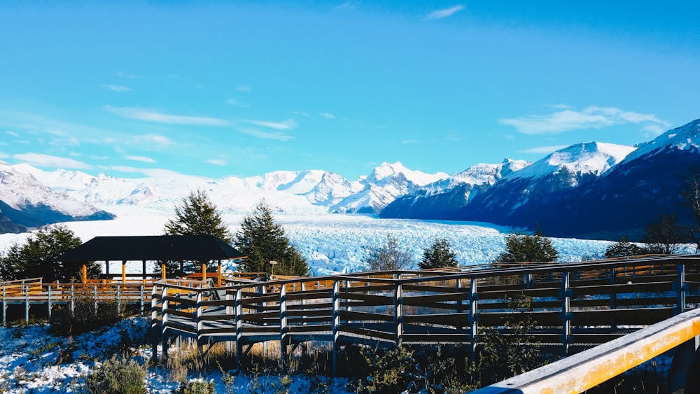 昼間、雪に覆われた山の近くの緑の芝生の上の茶色の木製の柵