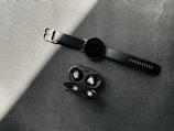 A variety of wireless earbuds and smartwatches arranged on a black surface with blue neon accents