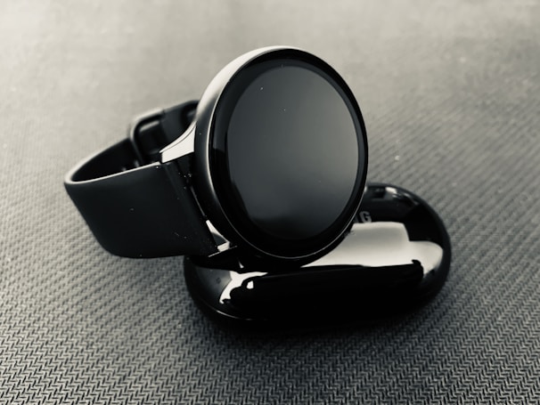 Smartwatch with a glossy black screen and gold frame, displayed on a reflective dark surface with subtle galaxy-themed lighting.