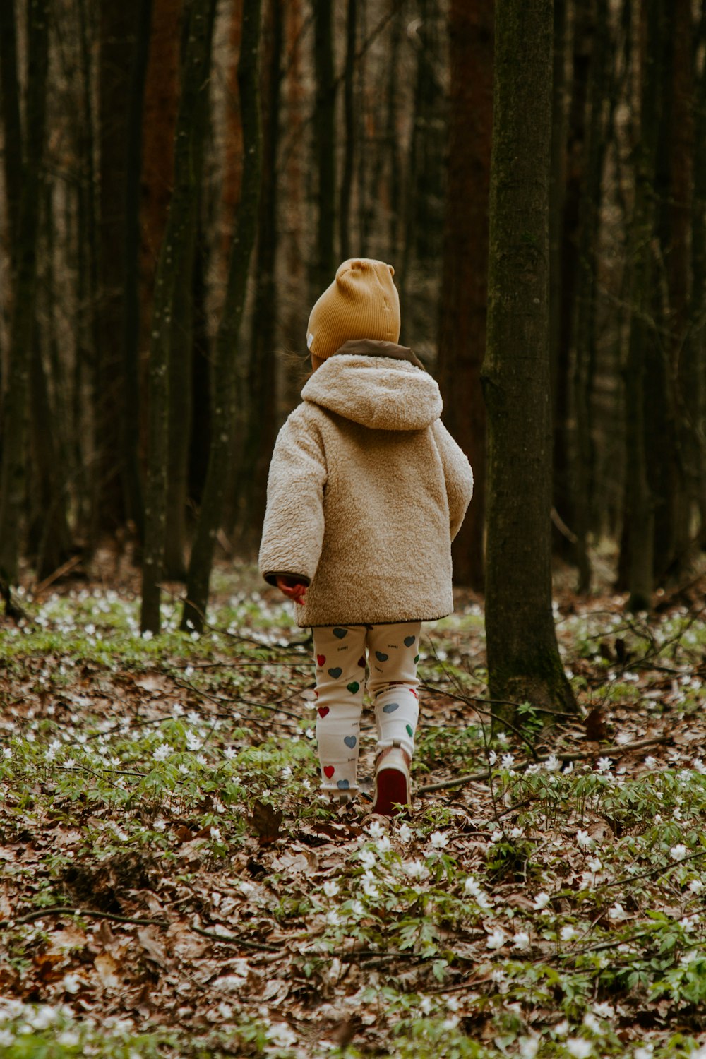 girl in pink coat and white pants standing on dried leaves on ground