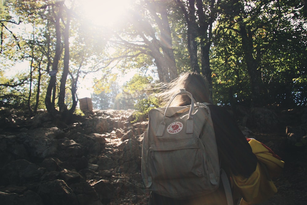 woman in black jacket and blue backpack standing near green trees during daytime