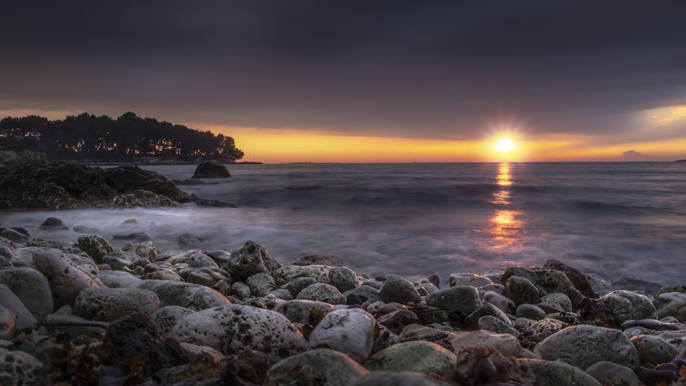 gray rocks near body of water during sunset