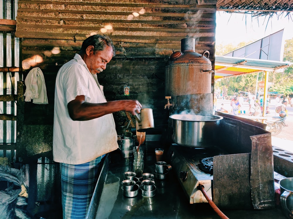 man in white t-shirt pouring water on stainless steel kettle