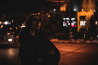 A moody, urban street scene at dusk featuring a person wearing cozy, dark-toned grindaura clothing.