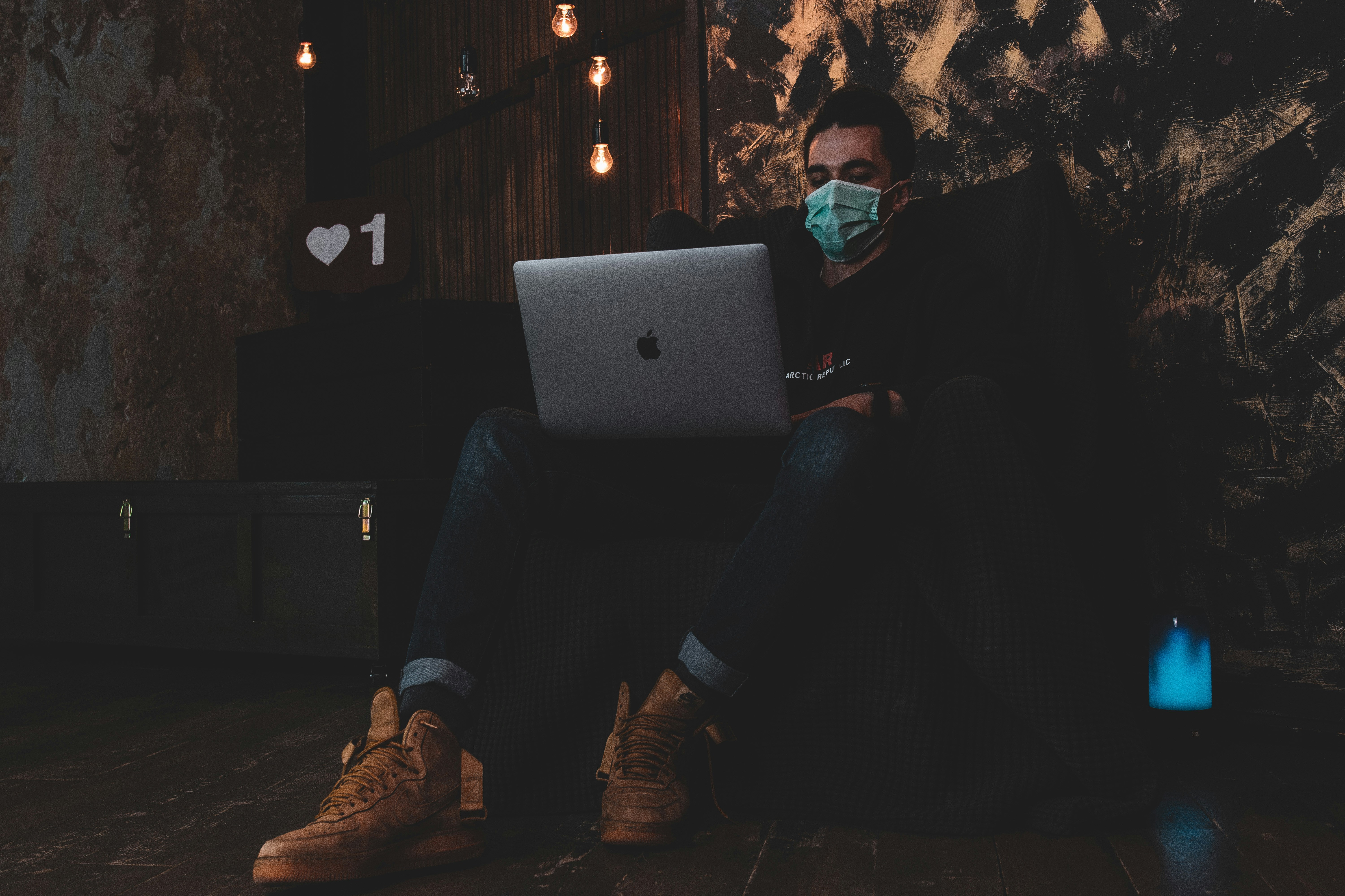 man in black jacket and black pants sitting on black couch using macbook