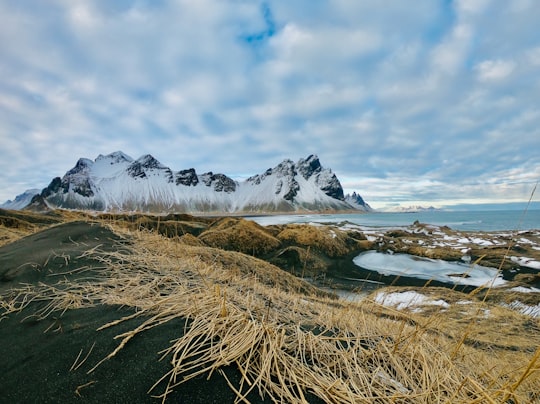 snow covered mountain near body of water under cloudy sky during daytime in Stokksnes Iceland