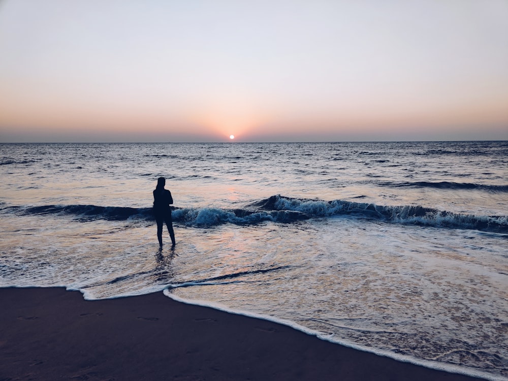 man in black wet suit standing on beach during sunset