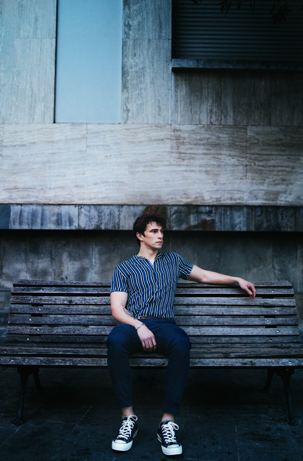 man in black and white striped shirt sitting on brown wooden bench