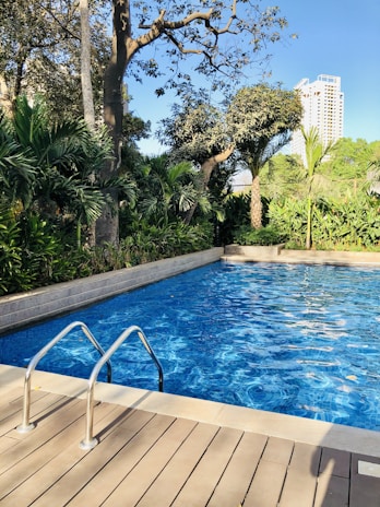 A sparkling clean pool surrounded by lush greenery under a clear blue sky.