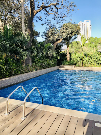 A sparkling blue swimming pool with clear water reflecting sunlight, surrounded by lush greenery.