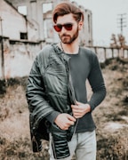 man in black leather jacket and blue denim jeans wearing black sunglasses