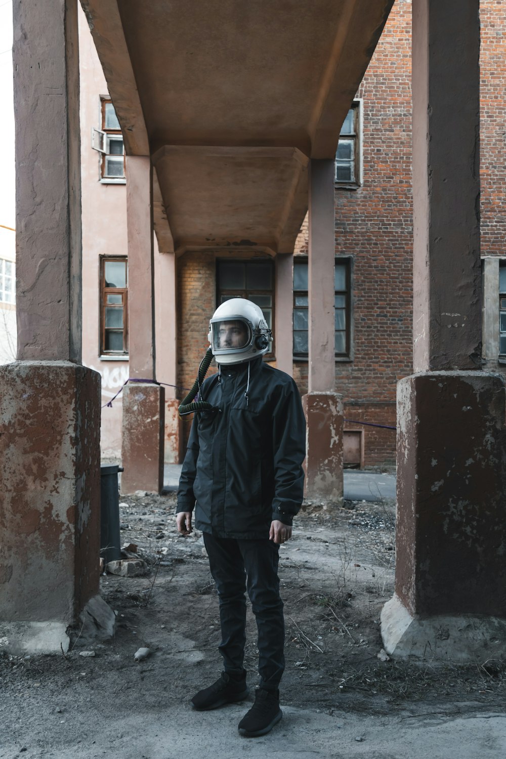 man in black jacket wearing white helmet standing beside brown concrete building during daytime