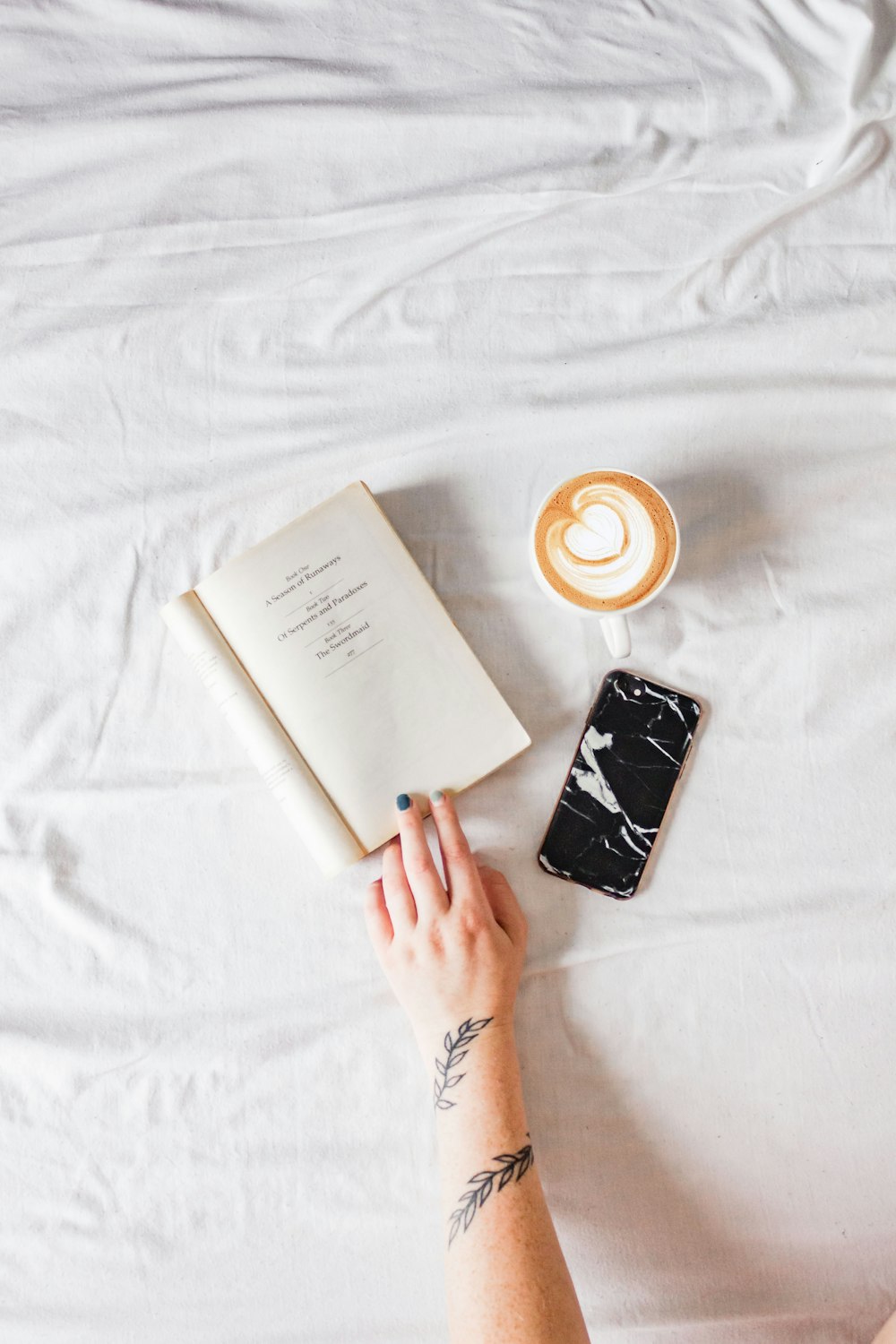 person holding white book beside white ceramic mug with coffee