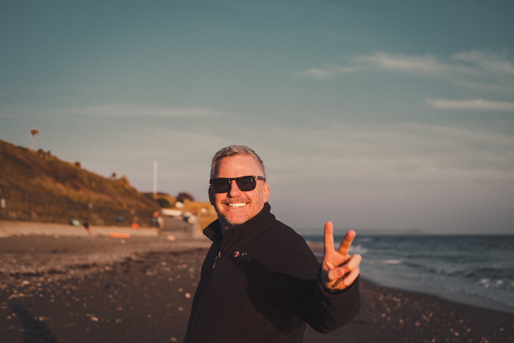 man in black jacket wearing sunglasses standing on beach during daytime