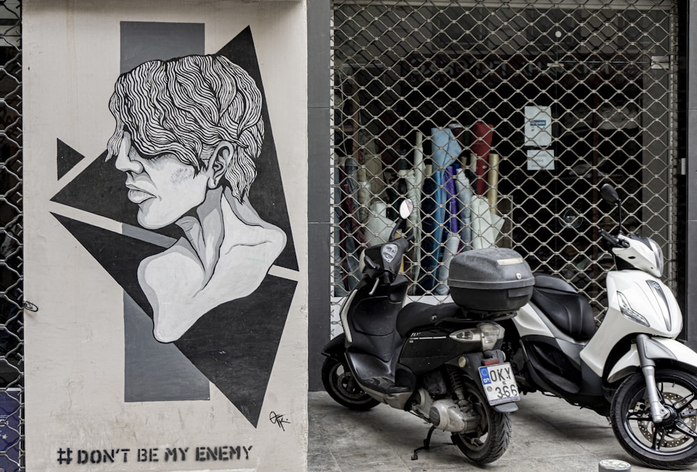 black and gray motor scooter parked beside wall with graffiti