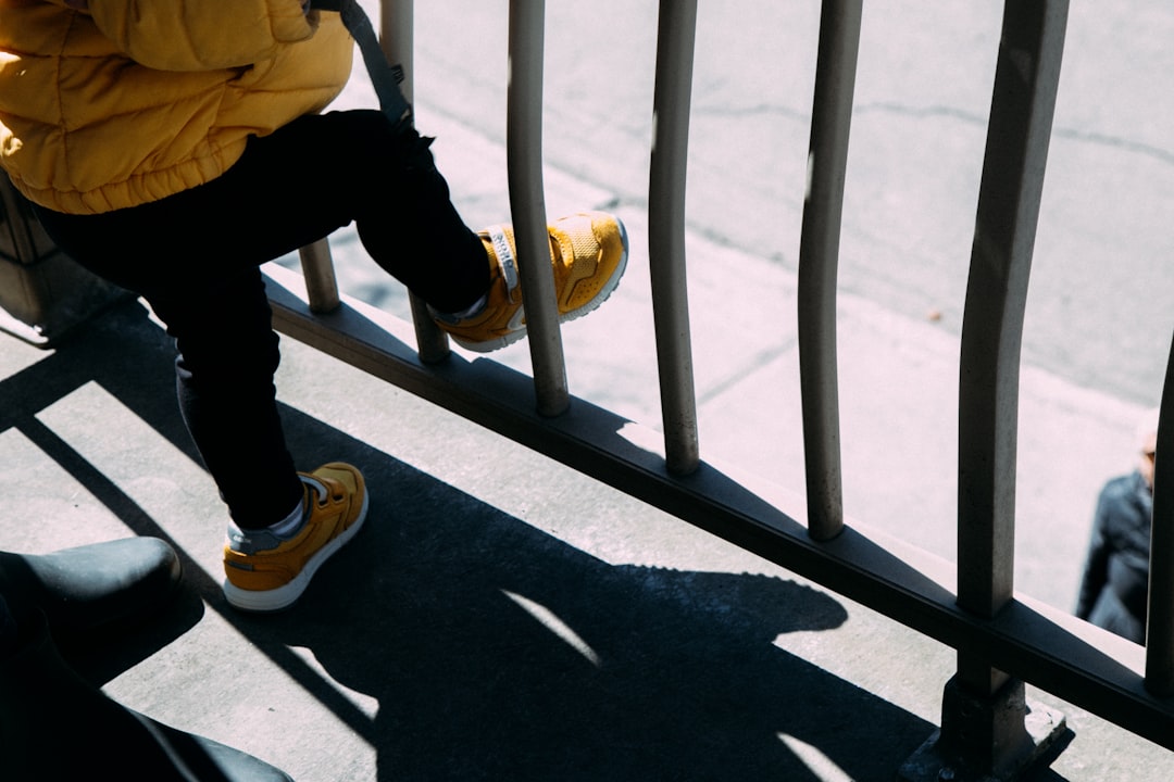 person in black pants and yellow hoodie walking on gray concrete road during daytime