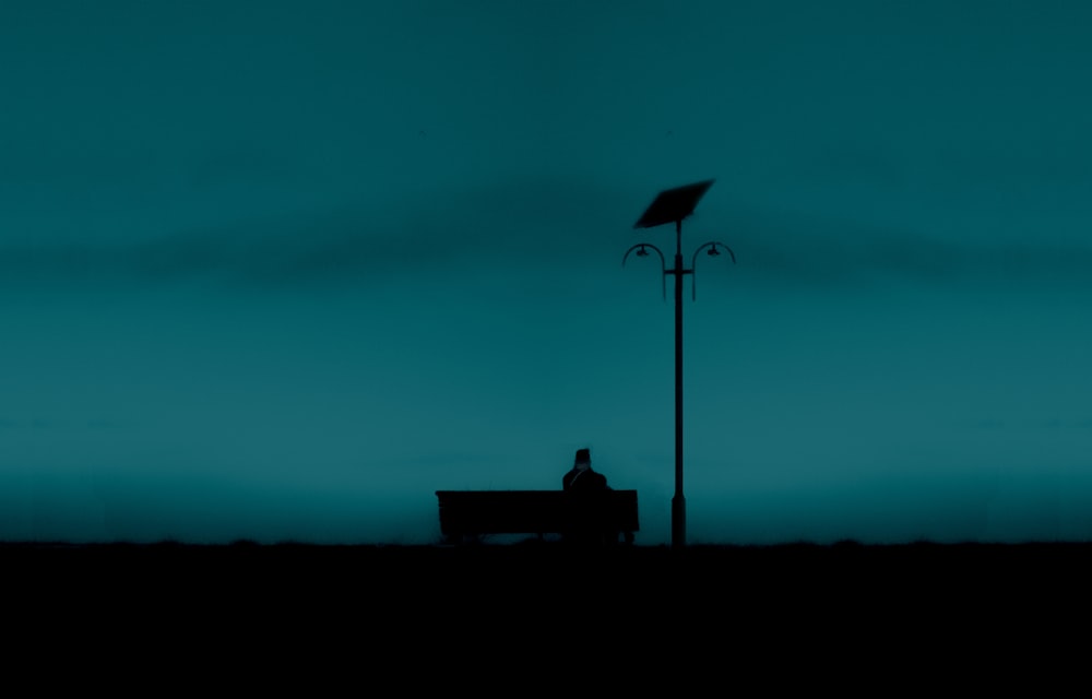 silhouette d’une personne assise sur un banc pendant la nuit