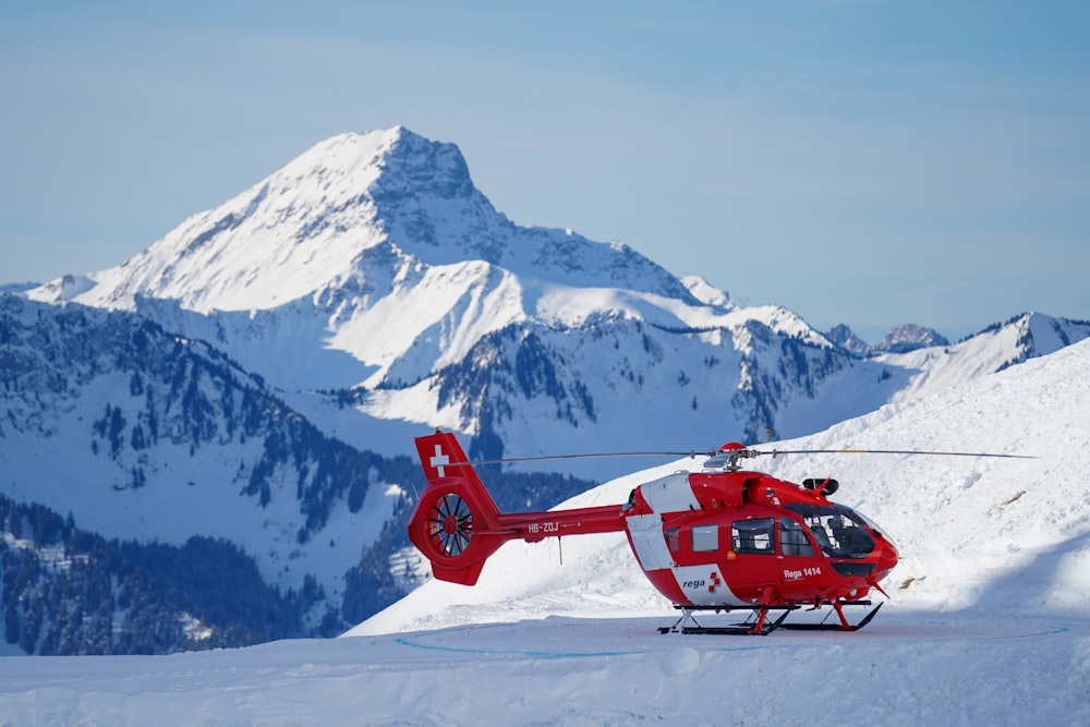 red helicopter flying over snow covered mountain during daytime