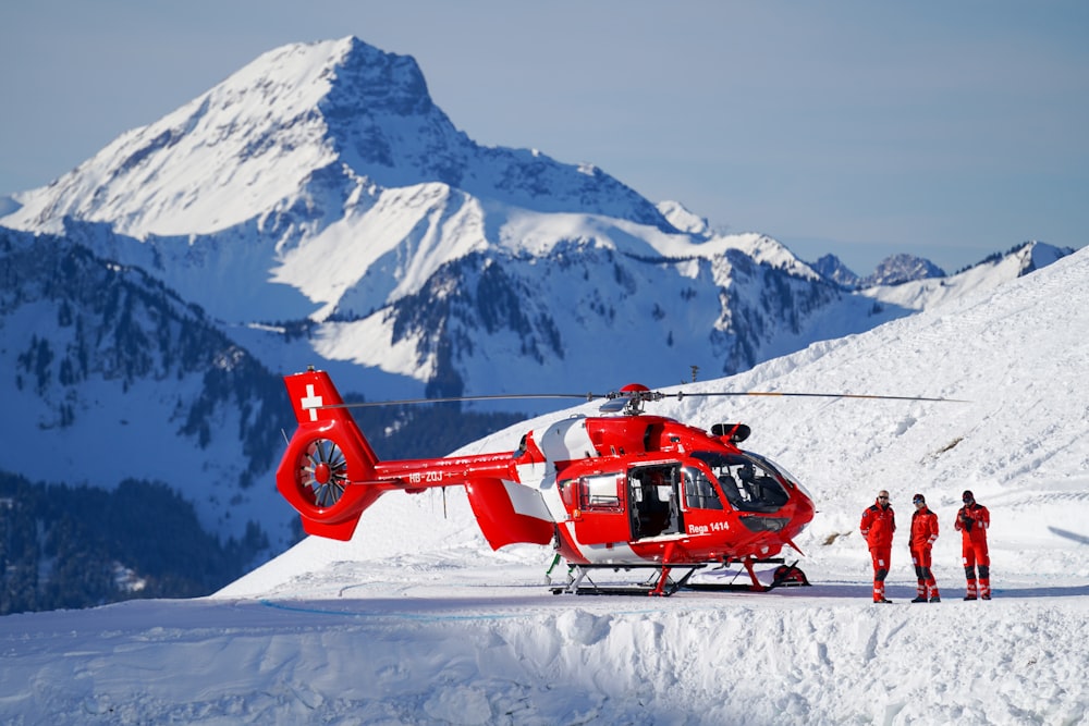 red helicopter flying over snow covered mountain during daytime