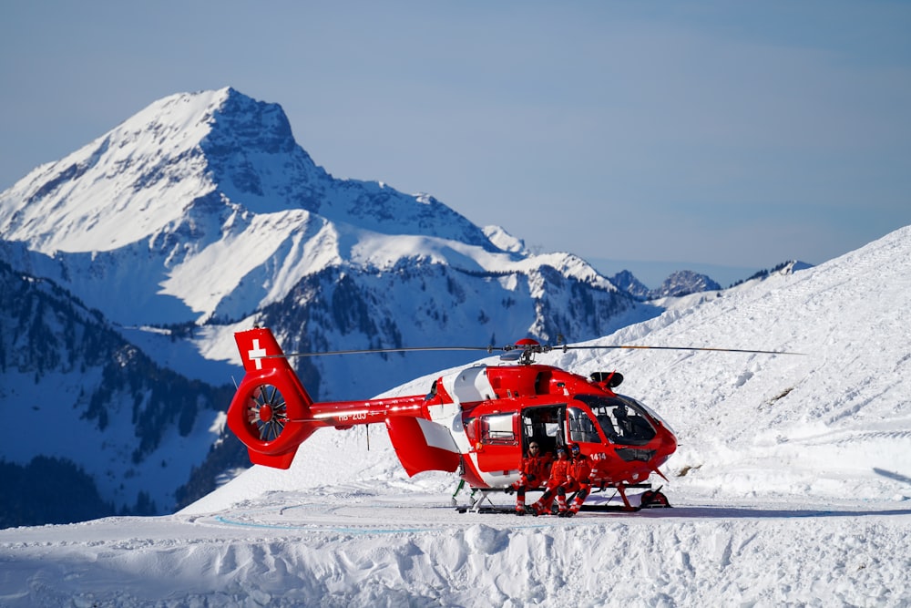 red and black helicopter flying over snow covered mountain during daytime