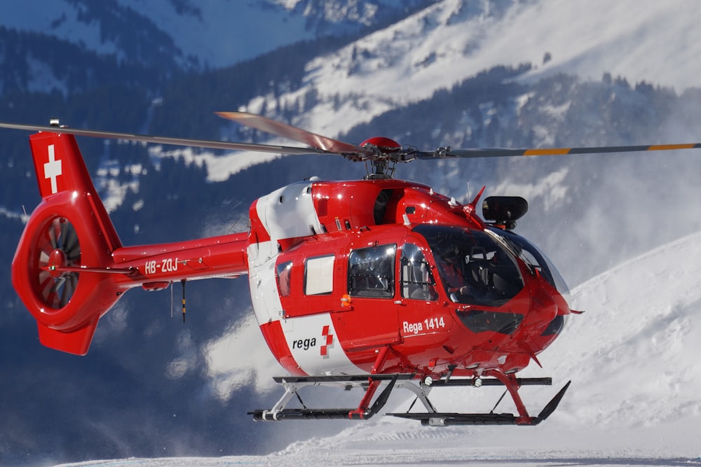 red and white helicopter flying over snow covered mountain during daytime