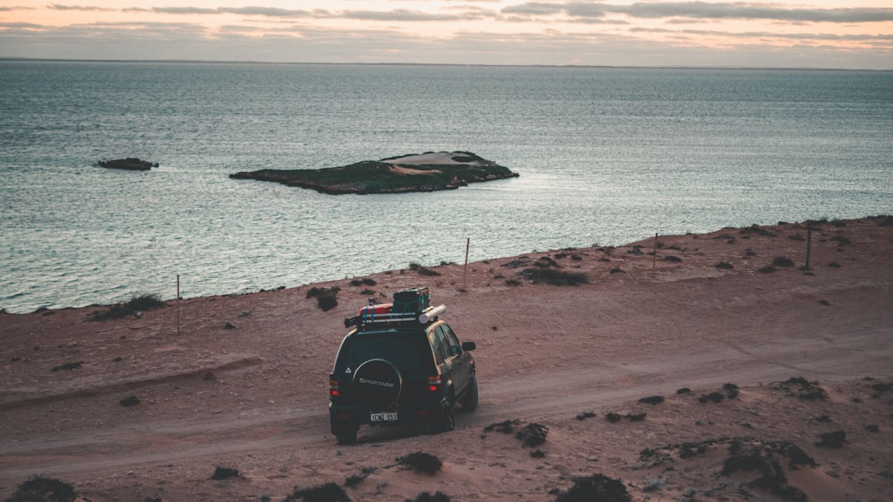 black suv on brown sand near body of water during daytime