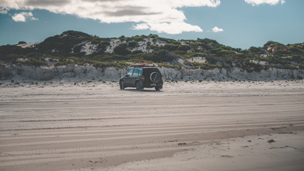 black suv on brown sand under white cloudy sky during daytime