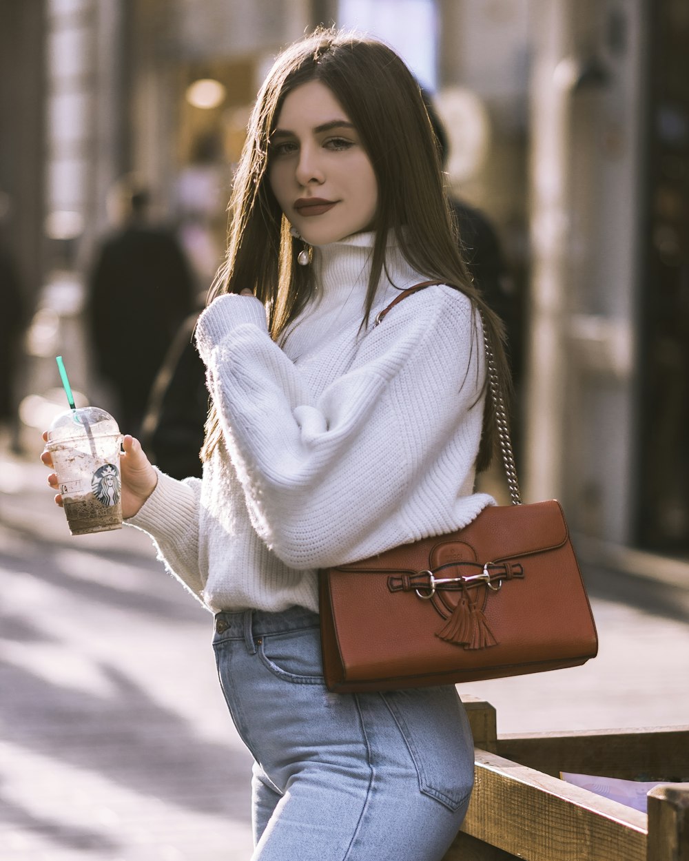 woman in white sweater and blue denim jeans holding clear plastic cup