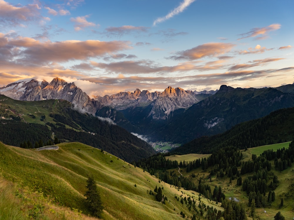 Grünes Grasfeld und Berge unter weißen Wolken und blauem Himmel tagsüber